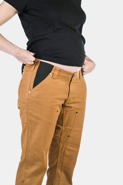 Side view of a woman wearing Dovetail Workwear's Anna Maternity Work Pants in Saddle Brown Canvas, showing the elastic panel and relaxed fit design