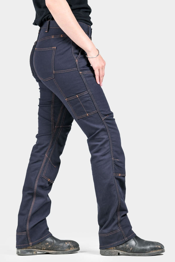 Back view of a woman wearing Dovetail Workwear's Britt Utility Pant in FR Navy Canvas, showcasing cargo pockets, reinforced knees, and straight leg fit with tough cuff detail.