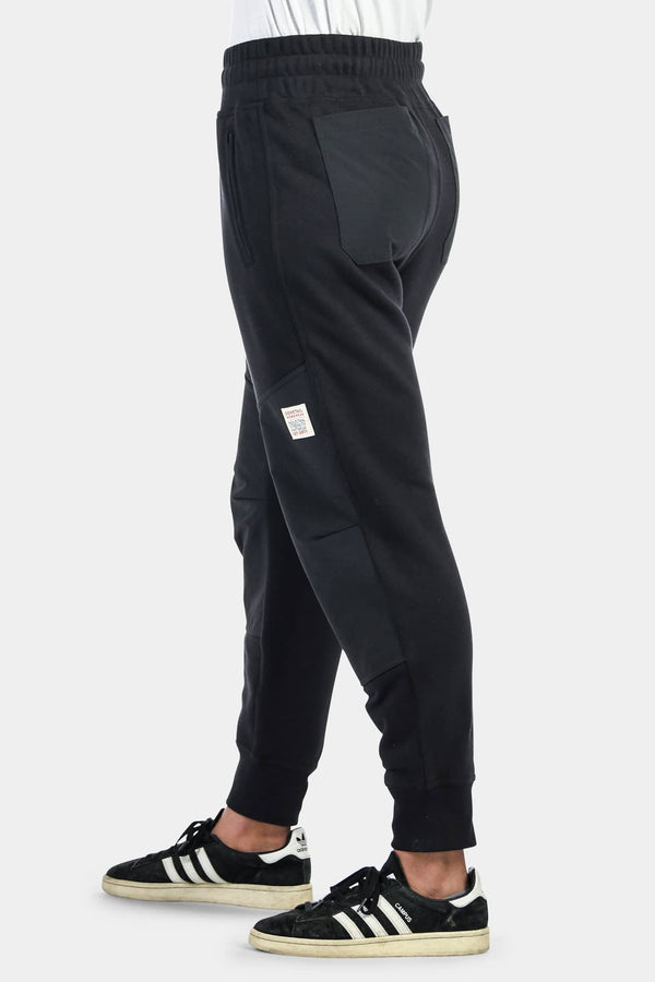 Side view of a woman wearing Dovetail Workwear's Flagger Fleece Jogger Work Pant in Black, showing reinforced knees and tapered leg design with elastic cuff.