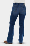 Back view of a woman wearing John Deere X Dovetail Workwear Into Town Bootcut Jeans in Classic Indigo Blue, showing reinforced back pockets and bootcut leg over work boots