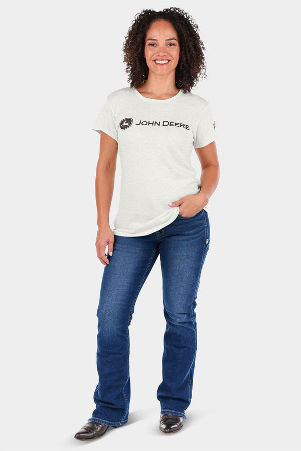 Woman wearing the John Deere X Dovetail Workwear Into Town Bootcut Jeans in Indigo Denim with a cream John Deere logo tee, posed against a white background