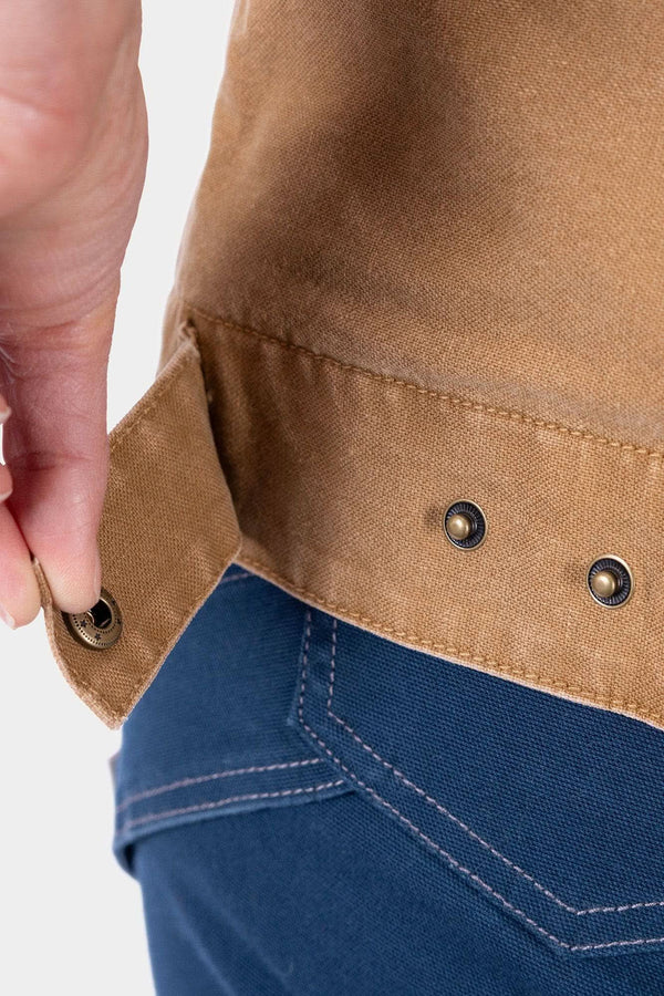 Close-up detail of the Dovetail Workwear Old School Trucker Vest in Vintage Brown, showing metal snap buttons and deep hand pocket on a woman wearing denim