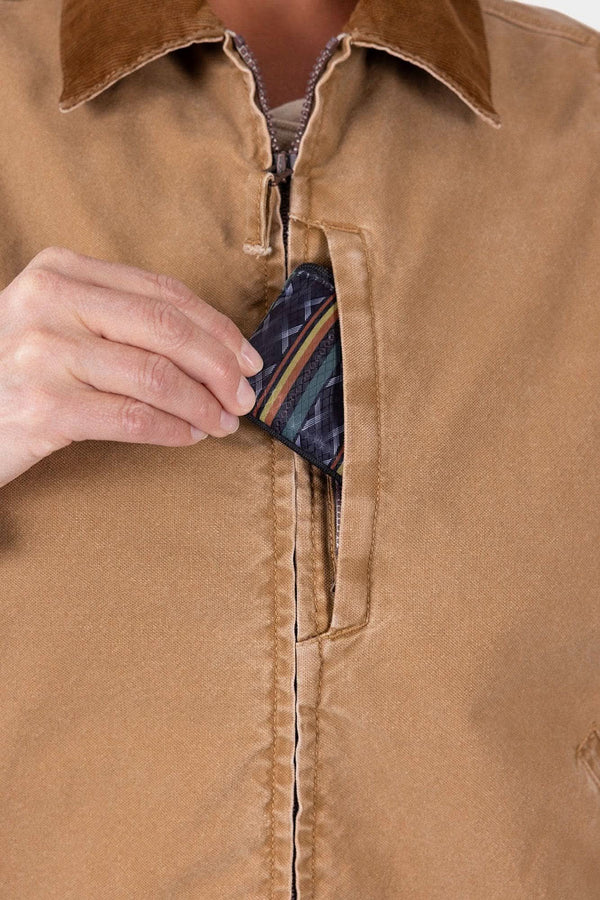 Detail of Dovetail Workwear's Old School Trucker Vest in Vintage Brown, showing the zip chest pocket and light quilted insulation visible inside as a woman reaches toward it