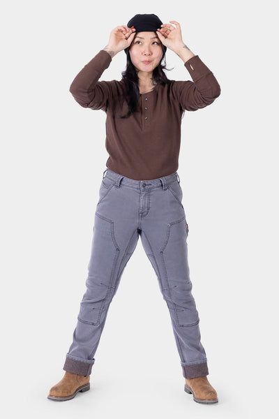 Woman wearing Dovetail Workwear Britt Utility HOTSWAP™ Pant in Grey Thermal Denim with brown henley and black beanie, standing with legs apart to showcase the straight-leg cargo-style pants
