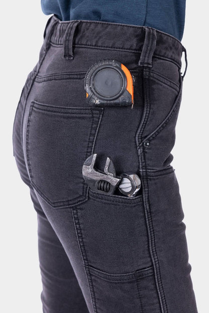 Side detail of Britt Utility HOTSWAP™ Pant in Black Thermal Denim showing tape measure slot in use, tools in pockets.
