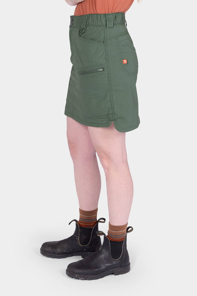 Side view of a woman wearing the Aventurine Green Compass COOLSWAP™ Cargo Skort by Dovetail Workwear, featuring visible bellowed zip cargo pockets and high-rise waistband