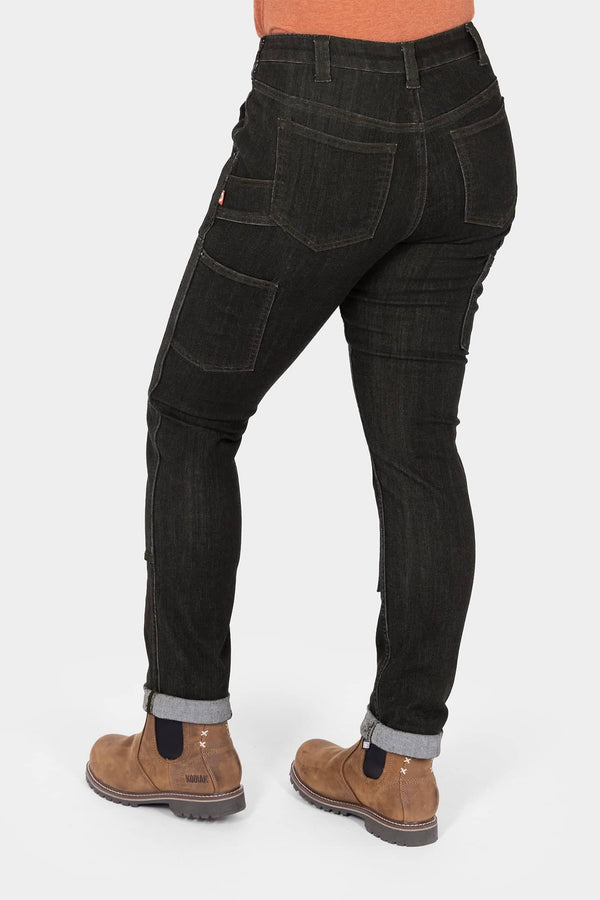 Back view of a woman wearing Dovetail Workwear's Maven Slim Pant in Heathered Black Graphene, showing cargo pockets, reinforced thigh panels, and cuffed inseam with work boots