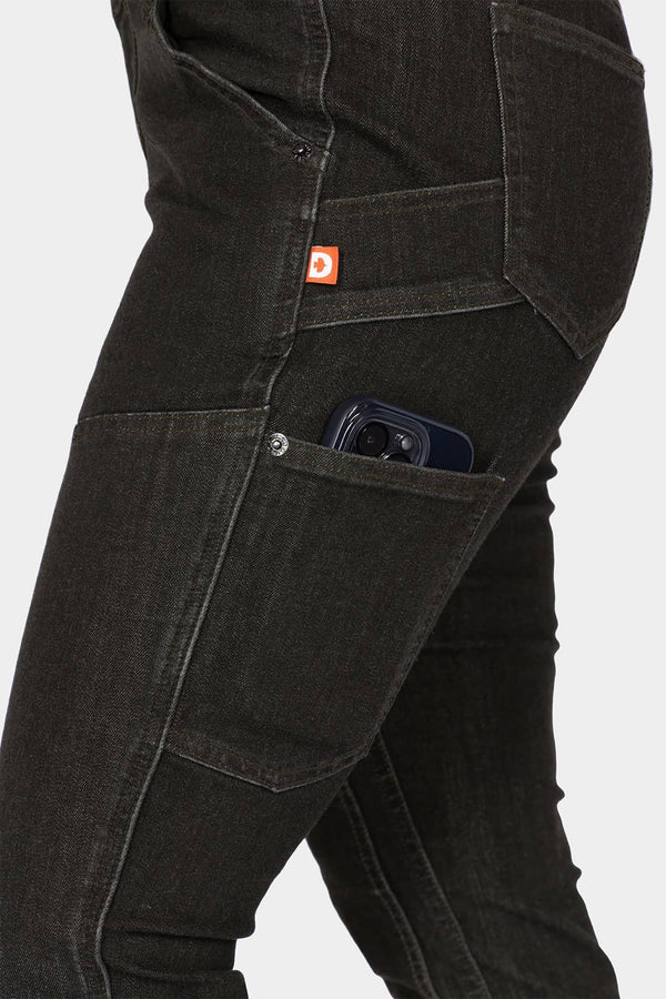 Side view of a woman wearing Dovetail Workwear's Maven Slim Pant in Heathered Black Graphene, showcasing the phone pocket and reinforced thigh panel with visible tool loop