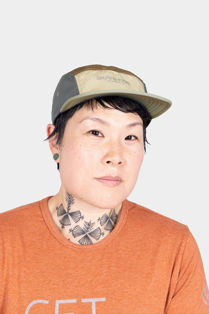 Dovetail Workwear Pack Cap in Desert Tan worn by a woman, showcasing the 5-panel construction, adjustable back closure, and breathable design of this classic work cap