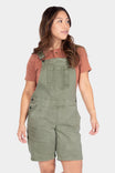 Dovetail Workwear Utility Short Overalls in Light Kelp Green worn by a woman with a rust t-shirt, featuring bib pocket with snap closure and flex suspenders