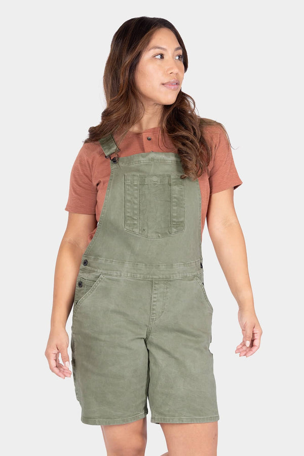 Dovetail Workwear Utility Short Overalls in Light Kelp Green worn by a woman with a rust t-shirt, featuring bib pocket with snap closure and flex suspenders