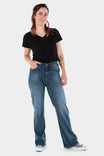 Woman wearing Dovetail Workwear's Old School Wide Leg Jeans in Classic Indigo Blue with a black v-neck tee and canvas sneakers, standing against a white background