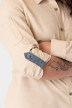 Detail view of the Ecru White Givens Long Sleeve Summer Work Shirt by Dovetail Workwear, showing the contrast cuff tab and sleeve pocket on a woman with a visible arm tattoo