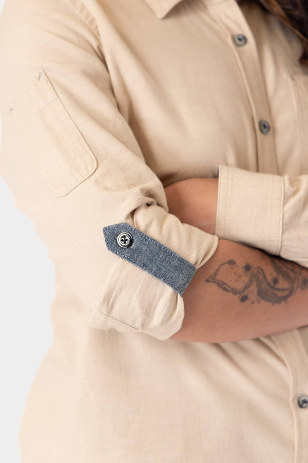 Detail view of the Ecru White Givens Long Sleeve Summer Work Shirt by Dovetail Workwear, showing the contrast cuff tab and sleeve pocket on a woman with a visible arm tattoo