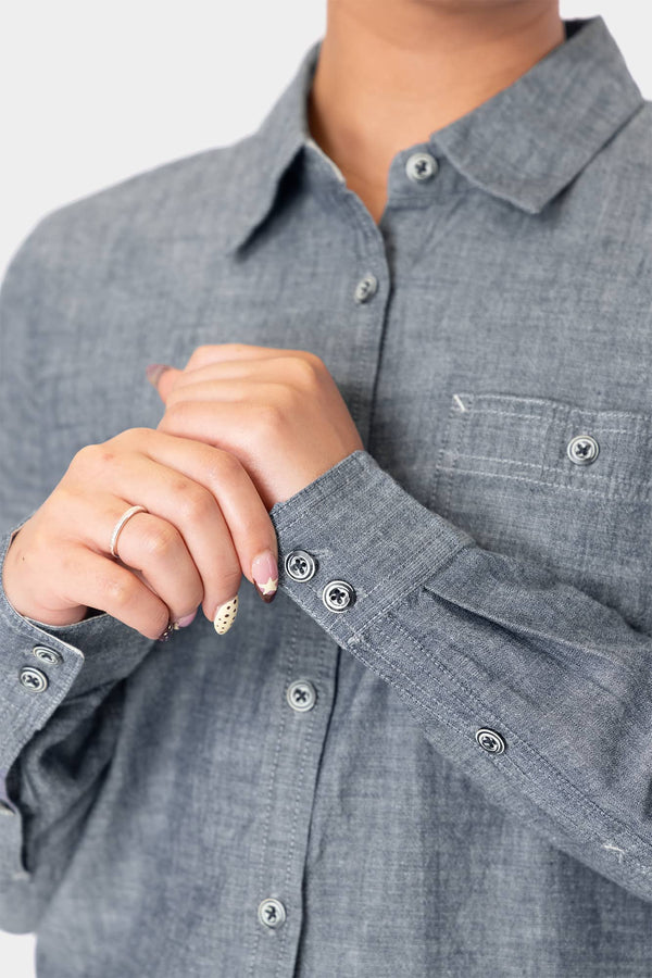 Detail of a woman's hands wearing the Dovetail Workwear Givens Long Sleeve Summer Work Shirt in Indigo Blue, showcasing the contrast inner cuffs and button chest pocket