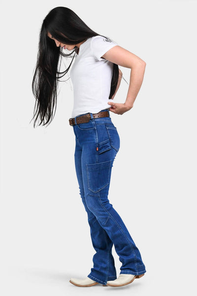 Side view of a woman wearing Dovetail Workwear's DX Bootcut Pant in Blue Sky Denim with a brown belt and white tee, showcasing the bootcut fit and tool loop