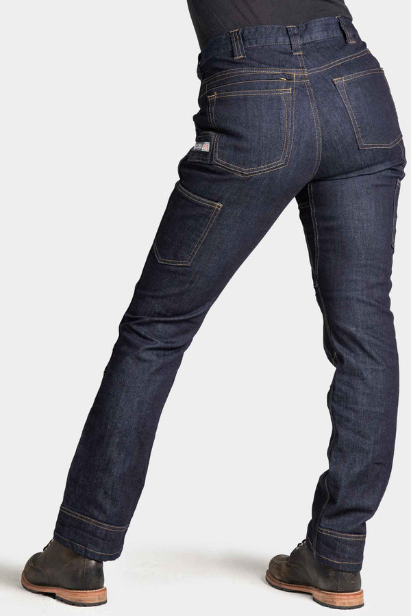 Back view of a woman wearing Dovetail Workwear's Britt Utility Pant in Indigo FR Denim, showing reinforced knees, cargo pockets, and straight leg fit with cuffed hem