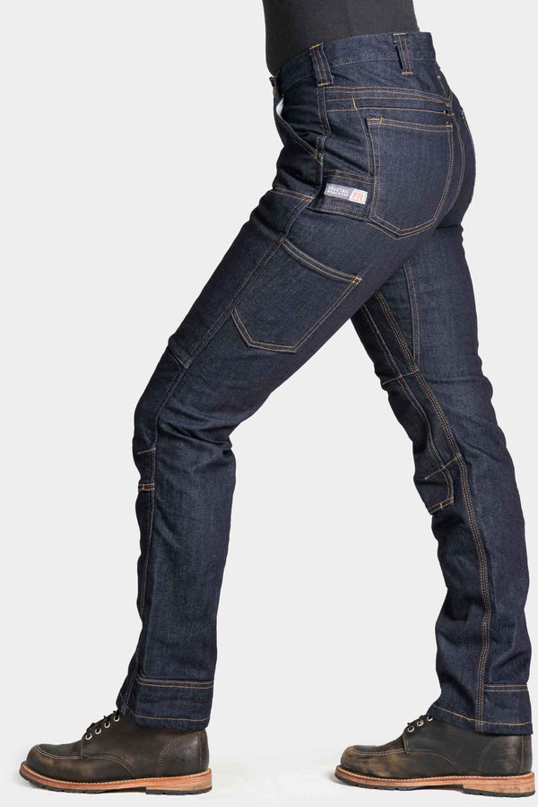 Side view of a woman wearing Dovetail Workwear's Britt Utility Pant in FR Denim, showing the straight leg fit, reinforced knees, and cargo-style pockets in Indigo.