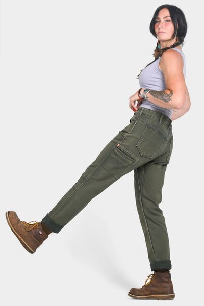 Woman wearing Dovetail Workwear Shop Pant in Olive Green Denim with relaxed leg and multiple pockets, paired with brown boots, shown in side profile pose against white background